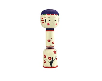 May include: A traditional Japanese wooden doll with a painted face and a blue and white hat. The doll is decorated with red flowers and black branches.