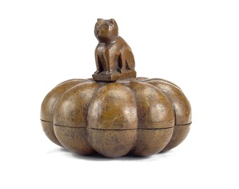 May include: A brown, pumpkin-shaped box with a carved cat figure on top. The box has a ribbed design and a hinged lid. The cat is sitting upright, with its ears perked up. The box is made of wood and has a natural finish.