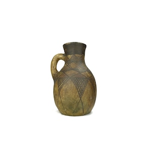 May include: A small, brown ceramic jug with a geometric pattern in black. The jug has a handle and a rounded body.