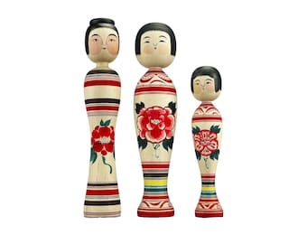 May include: Three traditional Japanese wooden dolls, known as kokeshi, with painted faces and floral designs. The dolls are standing in a row, with the tallest doll on the left and the shortest doll on the right.
