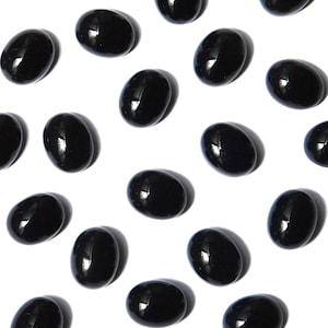 May include: A collection of glossy, oval-shaped black stones scattered on a white background. Each stone reflects light, creating highlights. The stones appear smooth and polished, with a consistent shape and size, suggesting they are uniform.