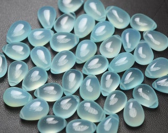 May include: A collection of pale blue teardrop-shaped gemstones. The polished stones have a translucent quality, with a subtle internal glow. The gemstones are scattered across a dark surface, creating a contrast that highlights their delicate color and form.