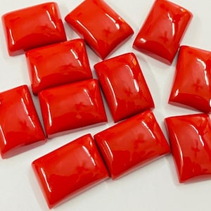 May include: A collection of rectangular, polished, bright red gemstones. The stones have rounded corners and a glossy finish, reflecting light. The arrangement suggests a collection of loose stones, possibly for jewelry making or crafting.