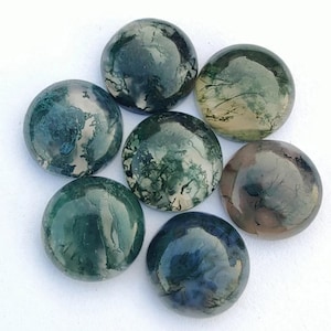Op de afbeelding: Zeven ronde, gepolijste mosagaat cabochons gerangschikt in een cirkelvormig patroon. De stenen vertonen een verscheidenheid aan groene, bruine en witte patronen, met een glanzende afwerking. De cabochons staan tegen een witte achtergrond.