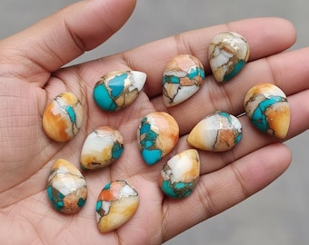 May include: A collection of teardrop-shaped gemstones with a mix of colors. The stones feature a vibrant turquoise, contrasted by shades of orange, white, and gold. The gemstones are displayed in a hand.