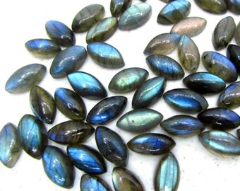 Puede incluir: Una colección de piedras preciosas de labradorita de forma ovalada. Las piedras muestran una gama de colores, incluyendo azules, verdes y grises, con destellos iridiscentes. Las piedras preciosas están dispersas sobre un fondo blanco, mostrando su belleza natural.
