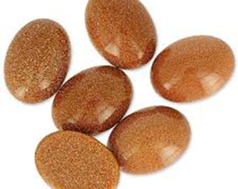 May include: Six oval-shaped, polished gemstones in shades of brown and gold are arranged on a white background. The stones have a smooth, glossy surface, with a speckled, textured appearance. These stones could be used for jewelry making.