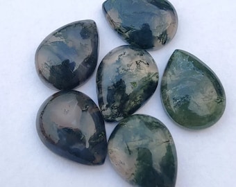 May include: Six polished moss agate gemstones in teardrop shapes. The stones display a mix of dark green, black, and translucent areas, with patterns resembling moss. The gemstones are arranged on a white surface.
