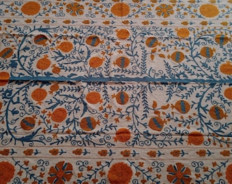 May include: A white fabric tablecloth with a blue and orange embroidered design. The design features stylized floral patterns and pomegranates.