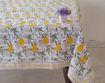 May include: White tablecloth with a lemon print. The tablecloth has a yellow and green border. A small white pot with purple flowers is on the tablecloth.