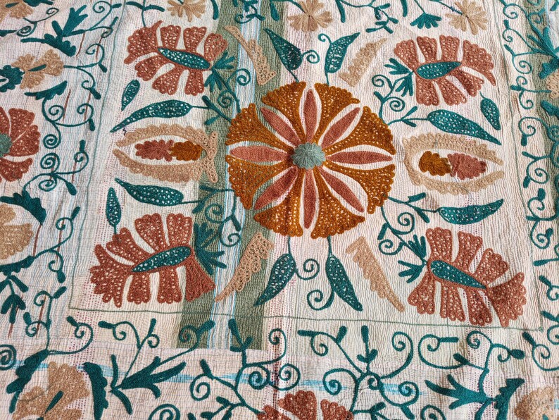 May include: Cream-colored textile with an embroidered floral pattern. The design features large, stylized flowers in shades of orange and brown, with teal and green accents. Intricate vines and swirls complete the design.