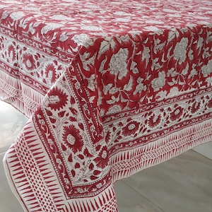 May include: Red and white floral tablecloth with a white background and a red floral pattern. The tablecloth has a border with a geometric design.