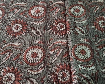 May include: A close-up of a textile with a floral pattern. The design features large, stylized flowers in shades of rust and white against a muted gray background. The fabric appears to be quilted, with visible stitching throughout.
