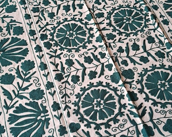 May include: Cream-colored textile with an embroidered floral pattern in teal. The design features large, circular flower motifs and smaller floral and leaf elements, creating a symmetrical and detailed pattern. The fabric appears to be cotton or linen.