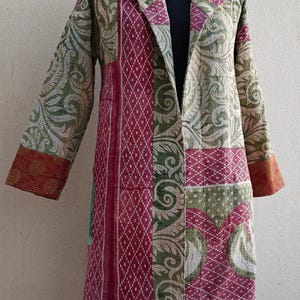 Może przedstawiać: Długa, pikowana kurtka w kolorze zielonym i różowym z kołnierzem szalowym. Kurtka wykonana jest z tkaniny patchworkowej z różnymi wzorami.