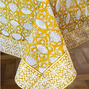 May include: Yellow tablecloth with a white floral pattern. The tablecloth has a border with a geometric pattern.