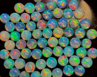 May include: A collection of round opals with a vibrant play of color. The opals display a range of hues, including blues, greens, reds, and yellows, creating a shimmering effect. The gemstones are set against a dark background.
