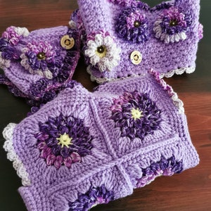 Könnte beinhalten: Lilafarbener Häkelkragen mit Blumendesign und Knöpfen. Der Kragen besteht aus mehreren Quadraten mit einer Blume in der Mitte jedes Quadrats.