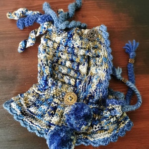 Peut inclure: Chapeau tricoté bleu et blanc avec un bouton marron qui dit "Hand Knitted" et un pompon bleu. Le chapeau a un long cordon bleu avec une perle marron.