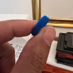 May include: A blue rubber ring with a textured surface. The ring is designed to help with grip and dexterity.