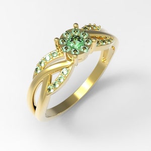 May include: A gold ring with a green gemstone surrounded by smaller green gemstones. The ring has a twisted band design.
