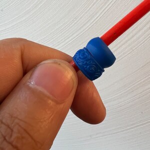 May include: A close-up of a blue and red plastic bead with a decorative design. The bead is threaded onto a red string.