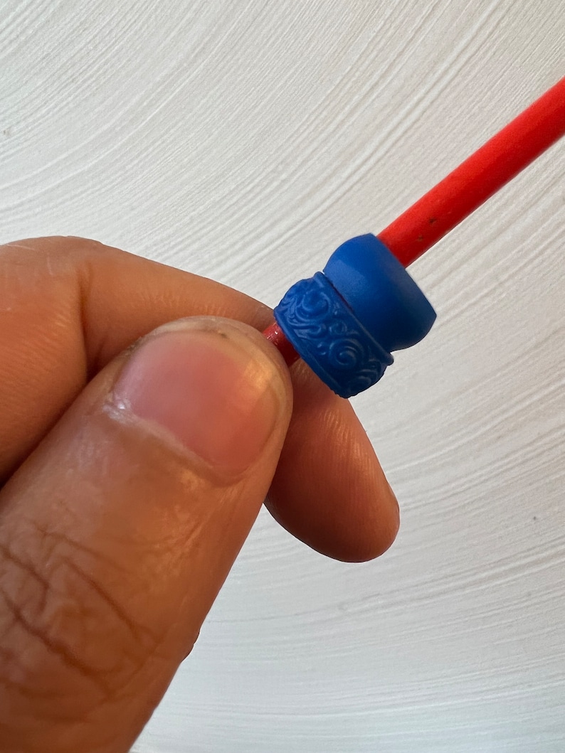 May include: A close-up of a blue and red plastic bead with a decorative design. The bead is threaded onto a red string.
