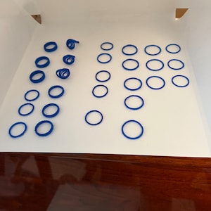 May include: A collection of blue plastic rings, some stacked and some scattered on a white surface.