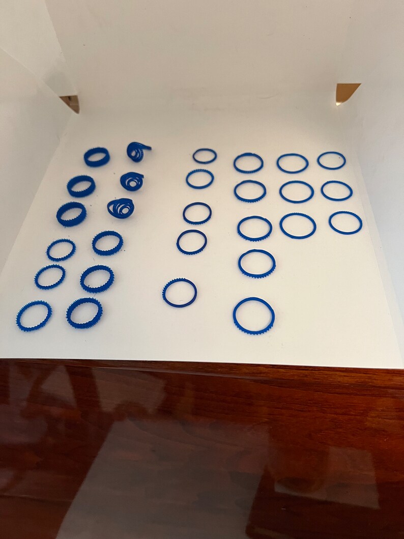 May include: A collection of blue plastic rings, some stacked and some scattered on a white surface.
