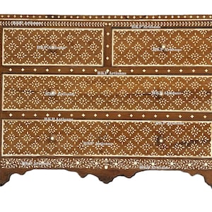 May include: A wooden chest of drawers with four drawers, featuring a floral inlay design. The chest is brown with white floral patterns and decorative trim. The text "BKP Artisans" is visible on the drawers.
