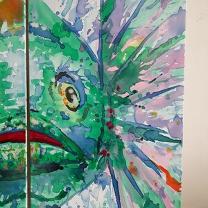 May include: Abstract watercolour painting showing a close-up of a green creature with a large eye and red mouth. The artwork uses a vibrant palette of green, blue, purple, and orange hues, with visible brushstrokes and splatters. The painting is on a white canvas.