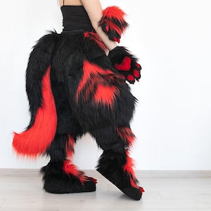 May include: A furry costume with black and red faux fur. The costume includes a tail, leg coverings, hand coverings, and foot coverings. The red fur is patterned throughout the black fur. The costume is designed to resemble a creature.