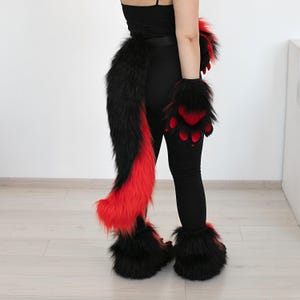 May include: A black and red furry costume set, including a tail, paw gloves, and foot covers. The tail is long and fluffy, with a black top and red bottom. The gloves and foot covers have black fur with red paw pads.