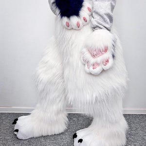 May include: A pair of white faux fur leg covers with black claws at the feet, paired with matching white and dark blue faux fur hand paws featuring pink paw pads. The set is worn with a light gray long-sleeve sweatshirt, creating a full-body costume.
