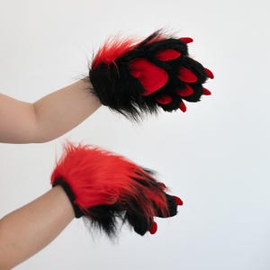 May include: A pair of furry paw gloves, featuring black fur with red accents. The paw pads and claws are a vibrant red. The gloves are designed to resemble animal paws.