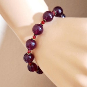 May include: A burgundy gemstone bracelet with small red beads and gold accents.