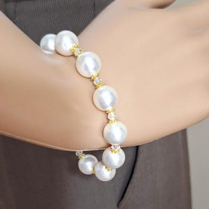 May include: A white pearl bracelet with gold accents and clear crystal beads.