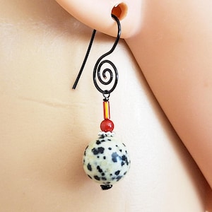 May include: A single dangle earring with a black hook and a decorative spiral. The earring features a speckled, round bead with black spots, red and yellow accents, and a small black bead at the bottom.