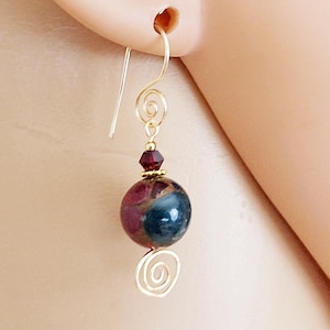 May include: Gold earrings with a dark blue and red gemstone bead, a small red crystal, and a gold spiral design.