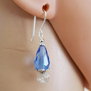 May include: Silver dangle earrings with a teardrop-shaped blue crystal and a silver swirl design.
