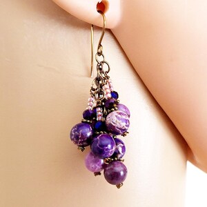 May include: Purple and pink gemstone dangle earrings with a bronze-colored metal chain and beads.