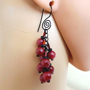 May include: A dangling earring with a black wire hook and a cluster of red beads. The earring features a spiral design at the top and a cascade of round, faceted red beads, accented with smaller black beads.