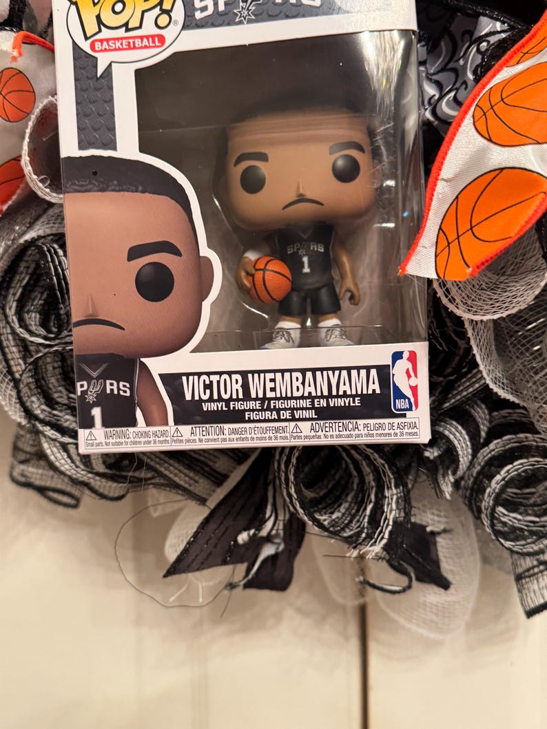 Puede incluir: Una figura de vinilo Funko Pop! de Victor Wembanyama con un uniforme negro y gris de los Spurs, sosteniendo un bal&oacute;n de baloncesto. La figura est&aacute; en una vitrina de pl&aacute;stico transparente. El embalaje incluye el logotipo de la NBA y las palabras "VICTOR WEMBANYAMA".