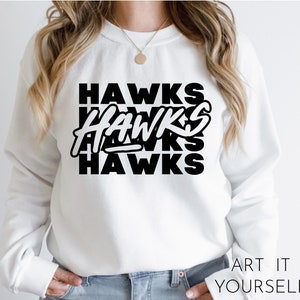 May include: White sweatshirt with black text that reads "HAWKS" three times, stacked on top of each other. The text is in a bold, blocky font.
