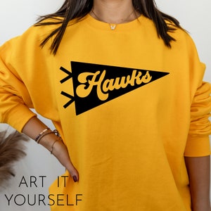 May include: Yellow sweatshirt with a black pennant design that says "Hawks" in a retro font.
