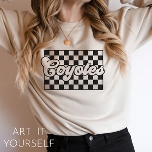 May include: A beige sweatshirt with a black and white checkered design and the word "Coyotes" in a retro font.