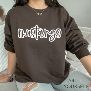 May include: A brown sweatshirt with the word "mustangs" written in white cursive lettering.