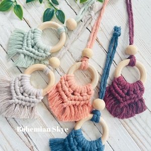 May include: Five handmade macrame keychains with wooden rings and tassels. The keychains are in various colors, including green, beige, peach, burgundy, and blue.