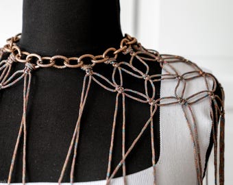 May include: A brown and white crocheted neckpiece with a copper chain. The neckpiece is made of a delicate, intricate pattern and has a flowing, cascading design.