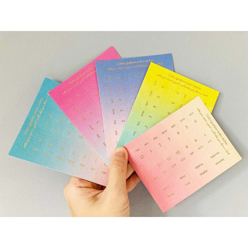 May include: A set of six colorful gradient index stickers with gold lettering. Each sticker features a different color gradient and a calendar layout with months and days of the week. The text on the stickers reads "Color gradient index stickies, what you want god lahat you have had."